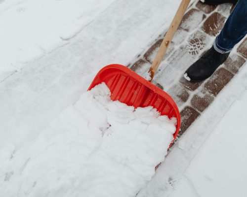 pexels photo 6952447 6952447 Person using a red snow shovel to clear snow from a driveway in winter.